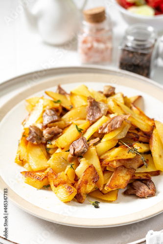 Fried potatoes with turkey meat and thyme in a plate on a white culinary background closeup