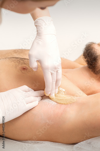 Young caucasian man receiving hair removal from his armpit in a beauty salon, depilation men's underarm