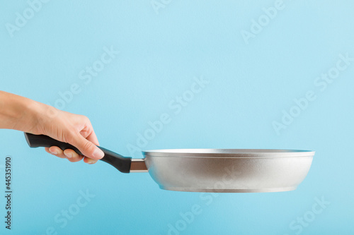 Photography Young adult woman hand holding new aluminium frying pan on light blue background