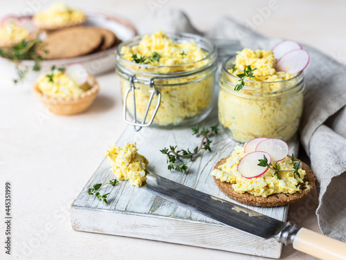 Tartlets with egg pate or salad and radish and thyme on light stone background. Egg dip in glass jar.