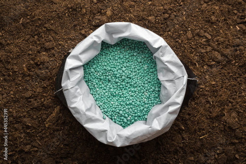 Bild auf Leinwand Opened plastic bag with green complex fertiliser granules on dark soil background