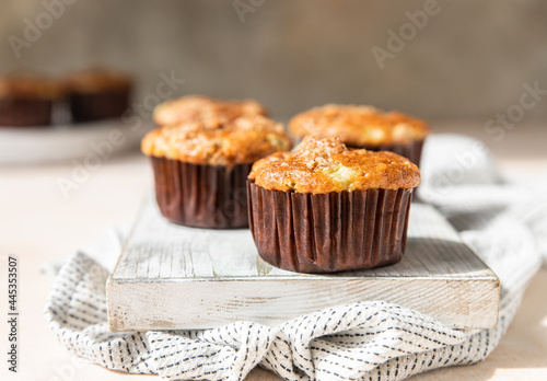 Tasty breakfast muffins with oat crumbs topping on white cutting board, light concrete background.