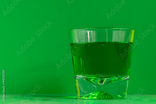 Glass with green drink on green background
