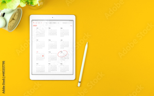 Tablet with September month 2021 calendar, yellow desktop background with copy space, top view photo