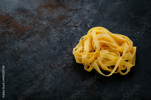 Natural Raw pasta fettuccine on a black stone background. Fresh uncooked egg Italian pasta, copy space