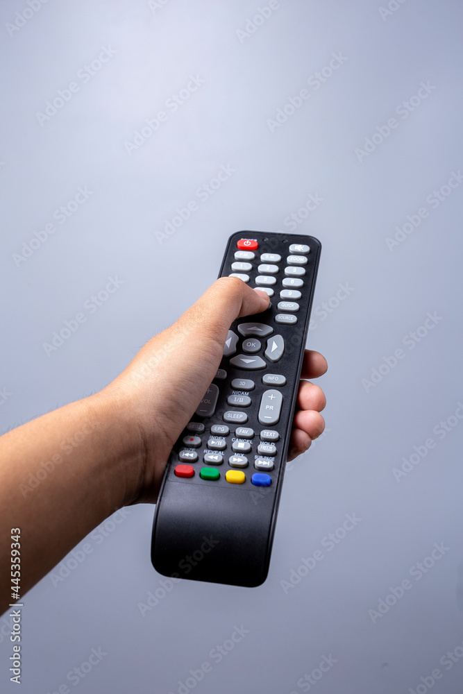 woman's hand holding TV remote control on gray background. woman's hand holding TV remote control on gray background.