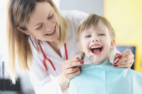 Dentist doctor examining teeth of little girl using instruments in clinic