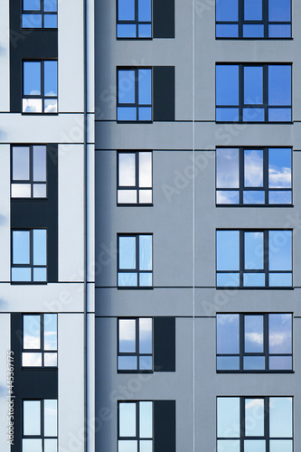 Facade of modern residential apartment building with reflection of cloudy blue sky in windows