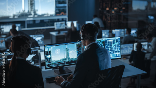 Group of People in Mission Control Center Witness Space Rocket Launch. Flight Control Employees Sit in Front Computer Displays and Monitor the Crewed Mission. photo