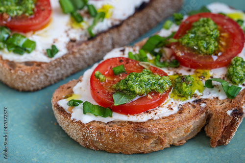 Delicious toasted bread with white cream cheese, green wild garlic and tomato on plate, close up