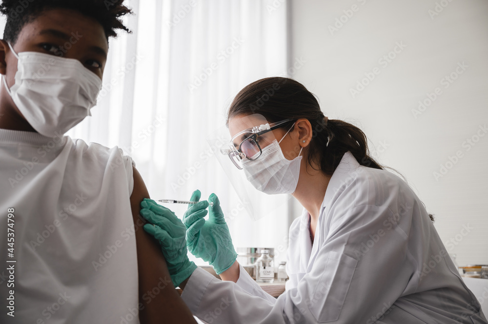A female doctor or nurse wearing mask,glove and face shield is injecting the coronavirus 19 vaccine on the shoulder of African-American man to immunize. Concept of preventing the spread of COVID-19. A female doctor or nurse wearing mask,glove and face shield is injecting the coronavirus 19 vaccine on the shoulder of African-American man to immunize. Concept of preventing the spread of COVID-19.