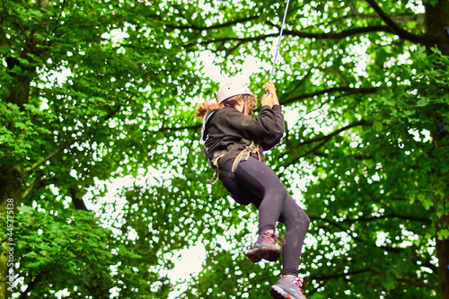 Young woman in safety equipment harness climbing and jumping from tree leap of faith on rope space for text