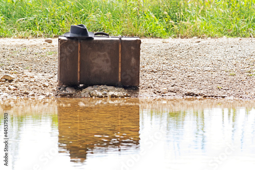 vintage suitcase with old hat and antique newspaper on dirt road , concept migration emigration voyage desertion moving