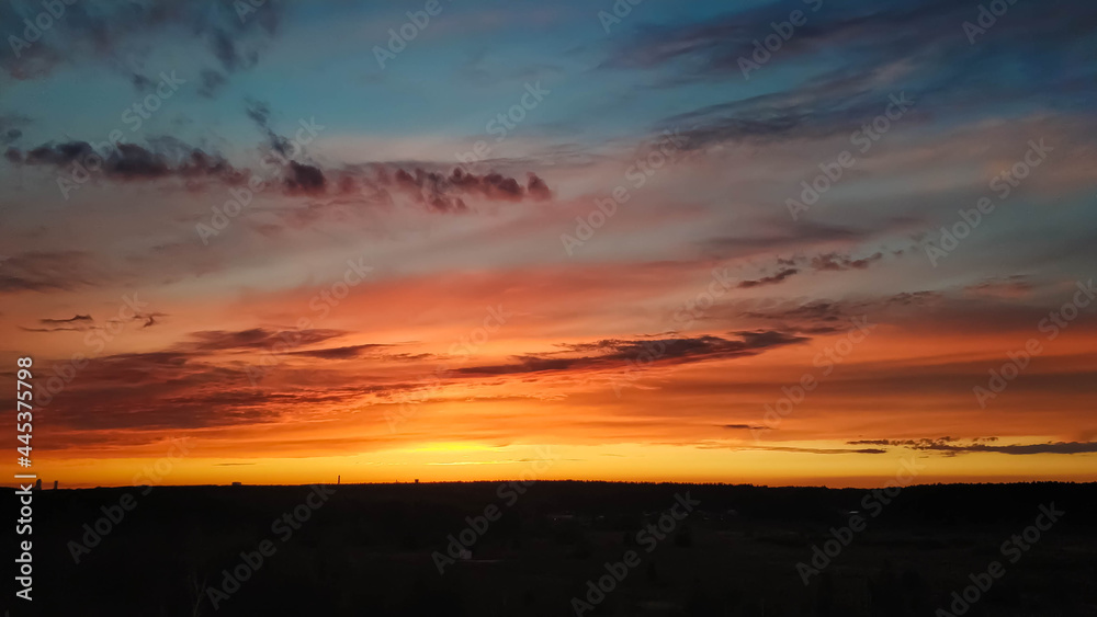Beautiful sunset over the field and forest. The sun is reflected in the clouds. View from above. Ural Russia 2021.