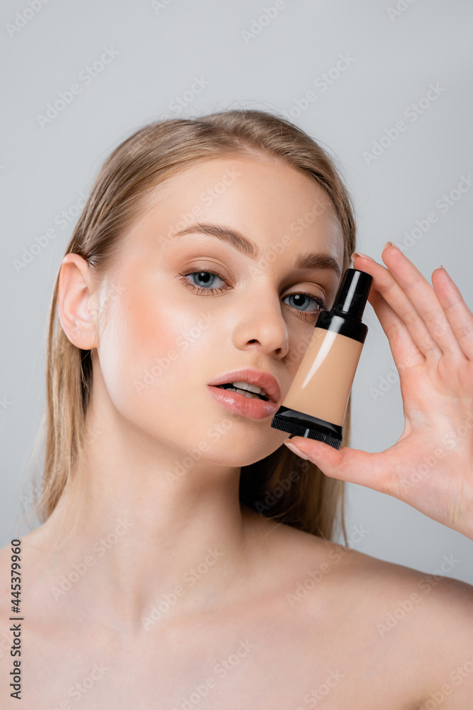 pretty woman with bare shoulders holding tube with makeup foundation isolated on grey pretty woman with bare shoulders holding tube with makeup foundation isolated on grey