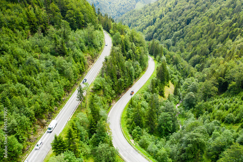 Aerial view of mountain road in the forest with moving cars and trucks. 