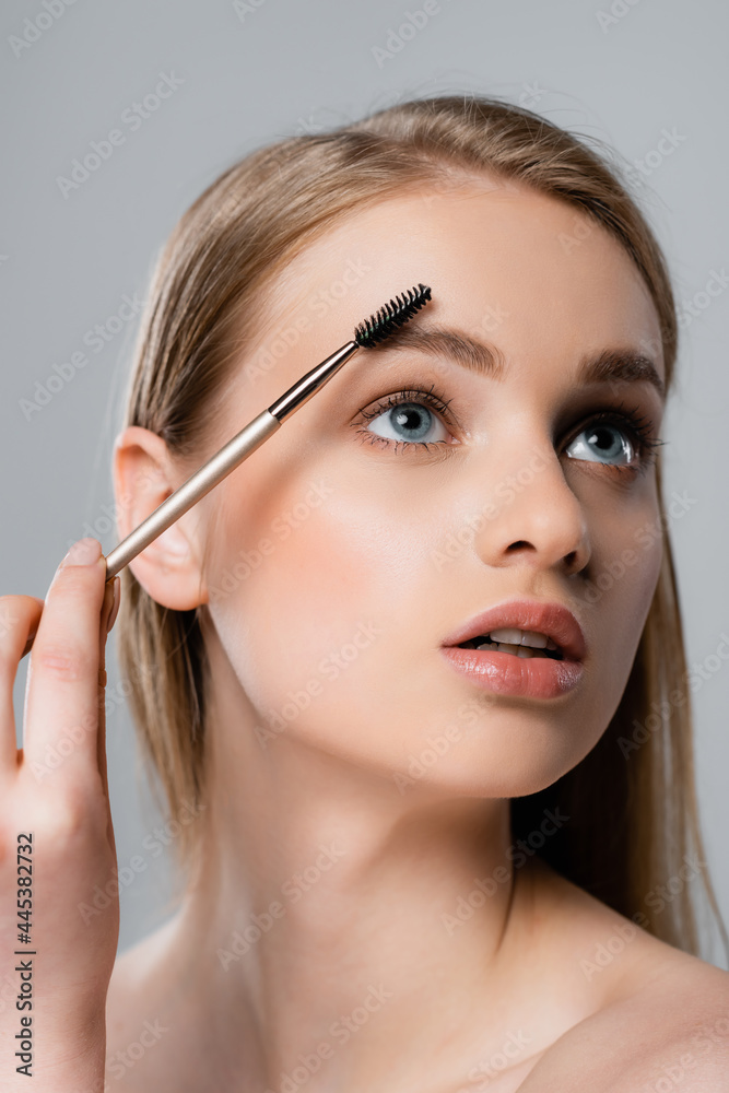 young woman with blue eyes styling eyebrow isolated on grey