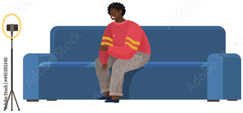 Man is recording video on smartphone. African american guy on sofa is broadcasting live, podcasting using phone. Record video, live online podcast. Male blogger broadcasting, recording video blog