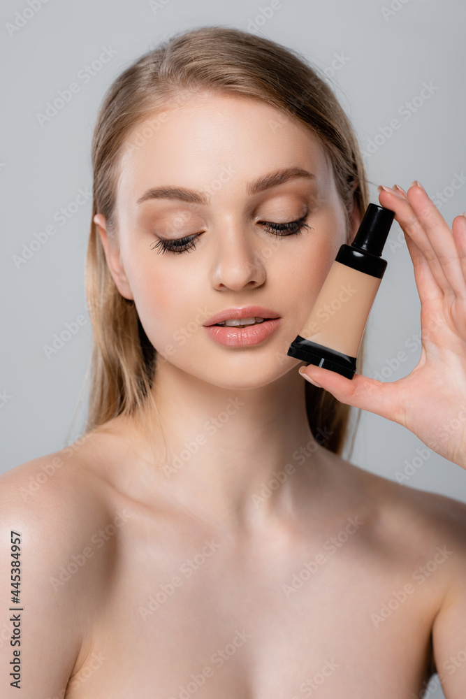 young woman with bare shoulders holding tube with face foundation isolated on grey young woman with bare shoulders holding tube with face foundation isolated on grey