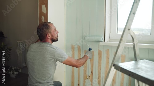 A man paints a wall with a roller. A man makes repairs in the room. Modern interior in the house. Beautiful design of the attic floor. Self-isolation. Quarantine. High-quality repairs