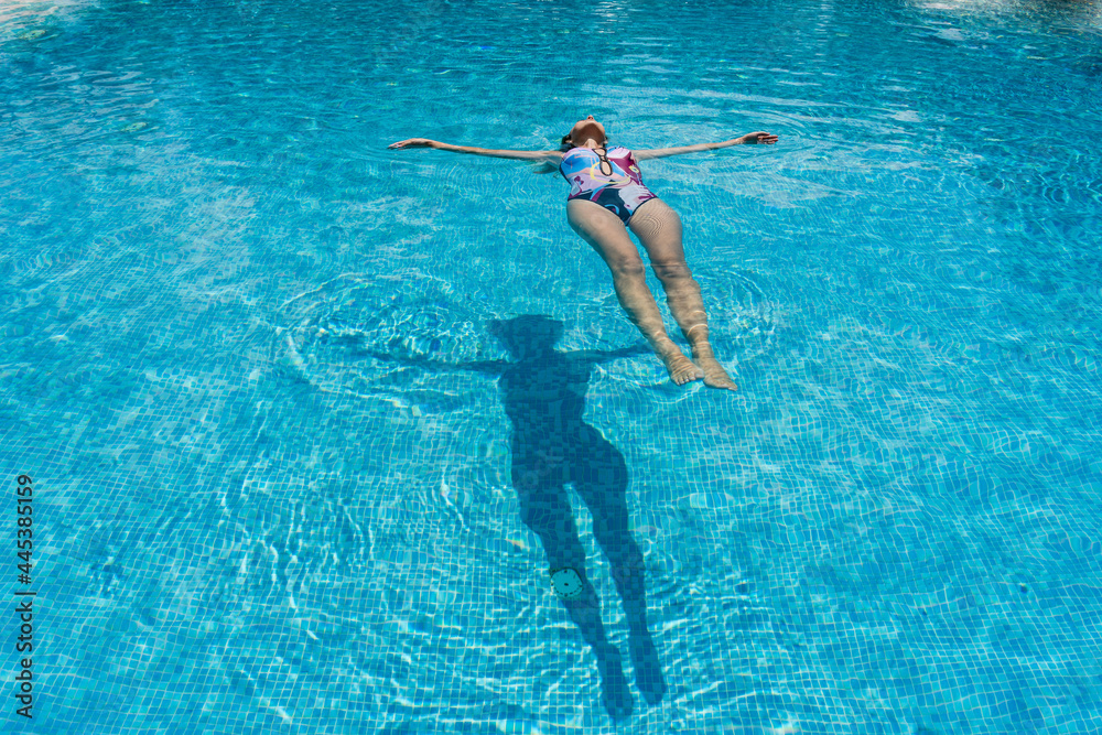 Slim woman lies on a water surface in the clear pool