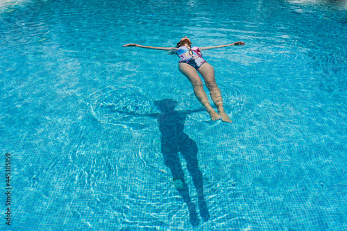 Slim woman lies on a water surface in the clear pool