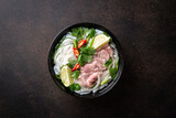 Traditional vietnamese soup Pho Bo with beef and rice noodles on a dark background, top view