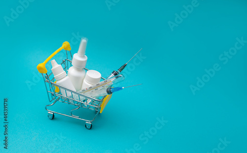 Shopping basket with medicinal pills, nasal spray, syringe and thermometer on a blue background. Pharmacy shopping concept. Home delivery of medicines
