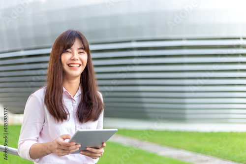 Happy young attractive business woman in her pink shirt using her tablet computer to check her social media outside of her office building © kudosstudio