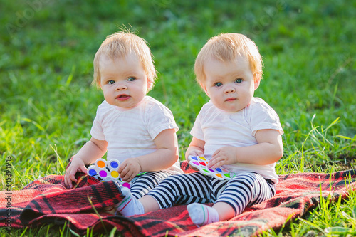 Two twin girls play with colored toys on a blanket on a sunny summer day.