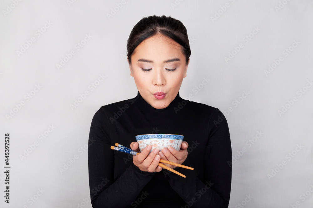 Oriental girl dressed in black blows the food inside her Chinese bowl with stick in your hands Oriental girl dressed in black blows the food inside her Chinese bowl with stick in your hands