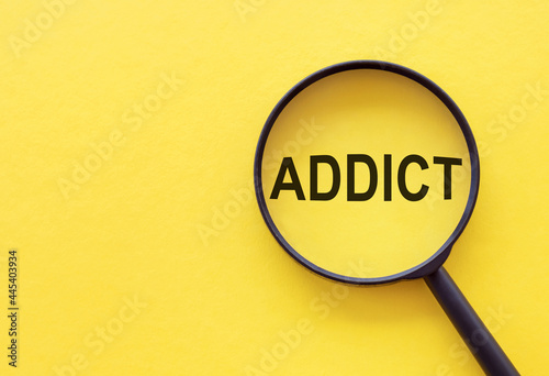 The word ADDICT is written on a magnifying glass on a yellow background.