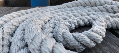 Sports and Recreation: Close-up of a white mooring line in several turns on a wooden pier.