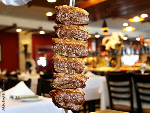 Picanha. Brazilian traditional steak in barbecue. Slices of grilled Picanha on a spit. Restaurant background. photo