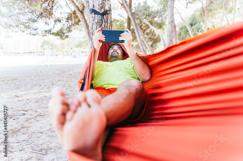 Hispanic man lying in a hammock and playing video games at Palmanova beach. Palma de Mallorca, Spain (Perfect for Copyspace)