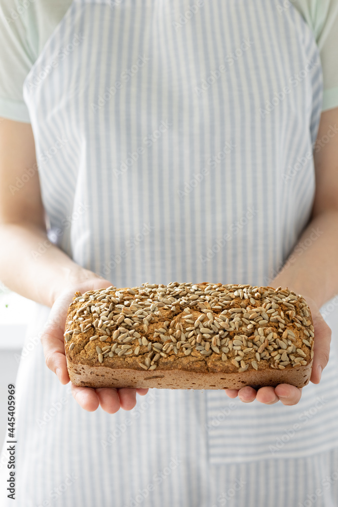 European woman baker holding buckwheat bread, white woman in a light apron holding homemade sourdough bread, sourdough bread, woman's hands cut bread for dinner, woman cook in bakery bakes vegetarian