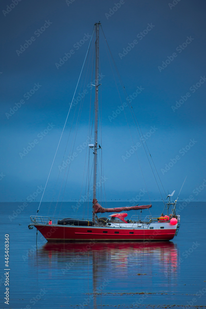 Anchored sailboat reflecting on the sea water on a cloudy day and blue background in Ushuaia, Tierra del Fuego, Argentina. Waters are of the Beagle Channel