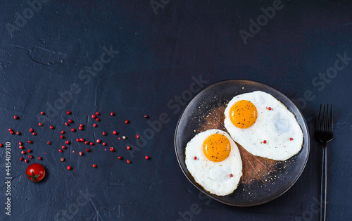 fried eggs in a pan on the black background with red pepper