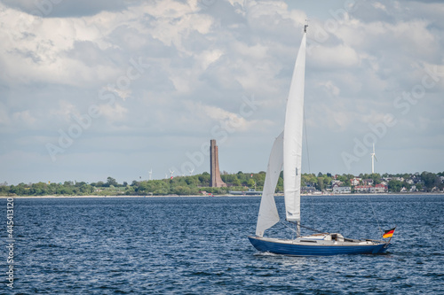 Germany, Schleswig-Holstein, Laboe, Lone sailboat sailing along Kiel Fjord with Laboe Naval Memorial in background photo