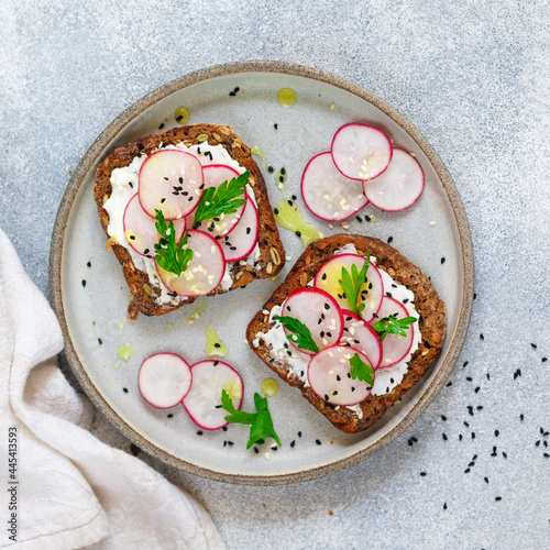 Healthy toasts of rye whole-grain bread with sunflower, flax and pumpkin seeds with cottage cheese (goat or ricotta), olive oil, fresh radishes, parsley and black and white sesame