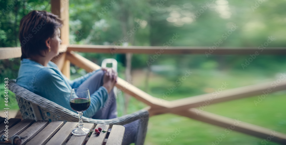 Lonely woman with a glass of wine looks into the garden on the veranda, depression and loneliness, banner Lonely woman with a glass of wine looks into the garden on the veranda, depression and loneliness, banner