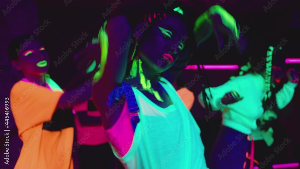 Group of female and male stylish dancers dancing inside dark place with neon lights .  Beautiful young people with fluorescent colorful make-up and clothes dancing in UV light. HD video in slow motion