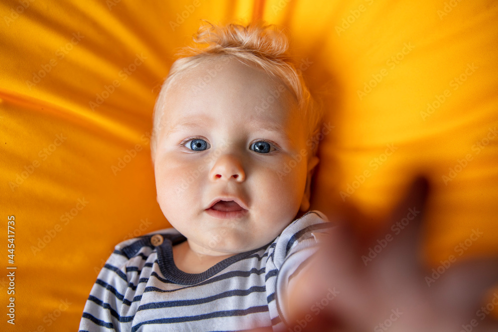 Close up of a cute 9 month old baby boy with blue eyes on a yellow background Close up of a cute 9 month old baby boy with blue eyes on a yellow background