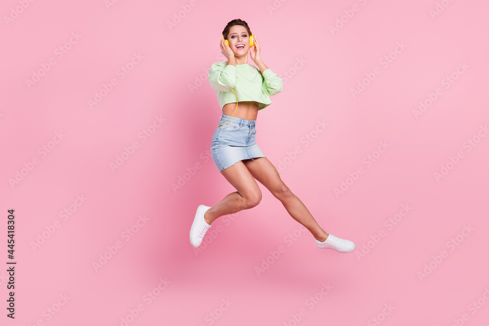 Full size profile side photo of young girl happy positive smile sound earphones jump up isolated over pastel color background Full size profile side photo of young girl happy positive smile sound earphones jump up isolated over pastel color background