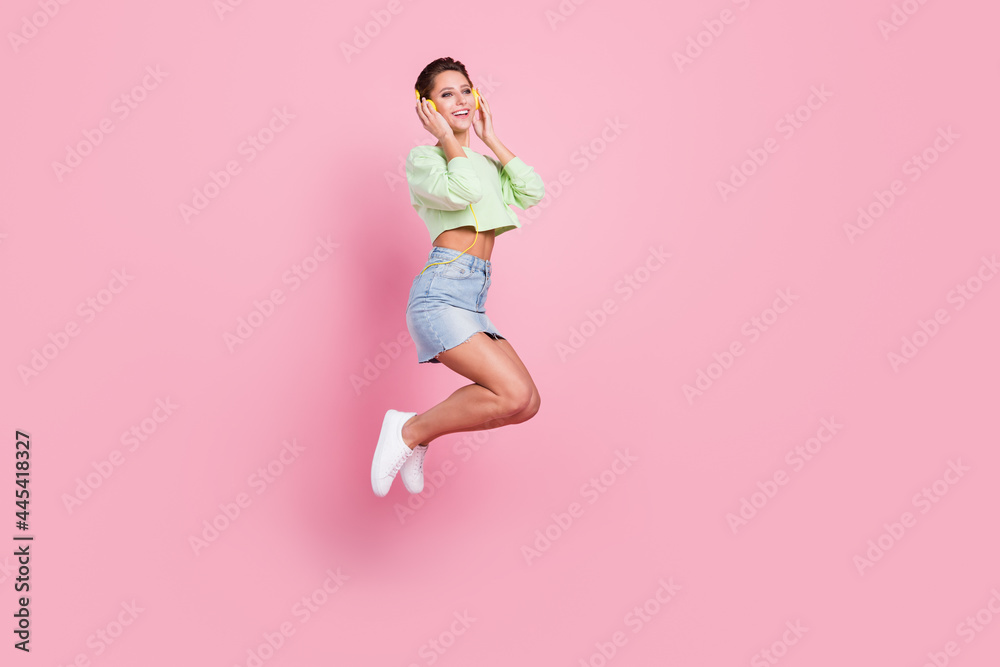 Full body photo of happy nice positive woman jump up smile listen music headset isolated on pink color background