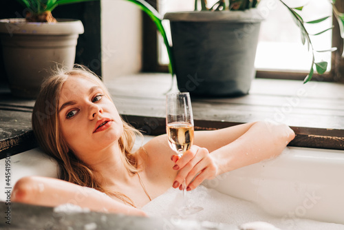 Beautiful young woman drinking champagne and looking to the camera enjoying bubble bath photo