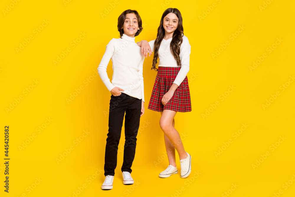 Full length body size photo of children smiling wearing stylish outfits isolated on vivid yellow color background Full length body size photo of children smiling wearing stylish outfits isolated on vivid yellow color background