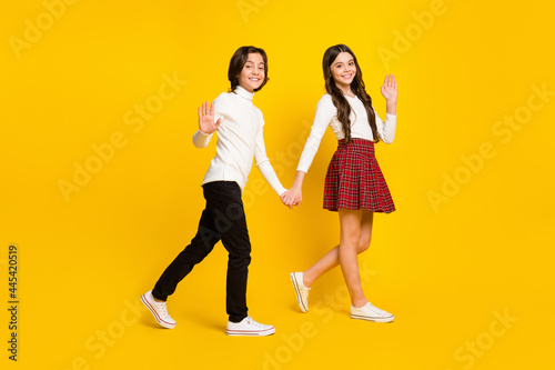 Full length body size side profile photo of children holding hands going to school waving hands isolated vibrant yellow color background