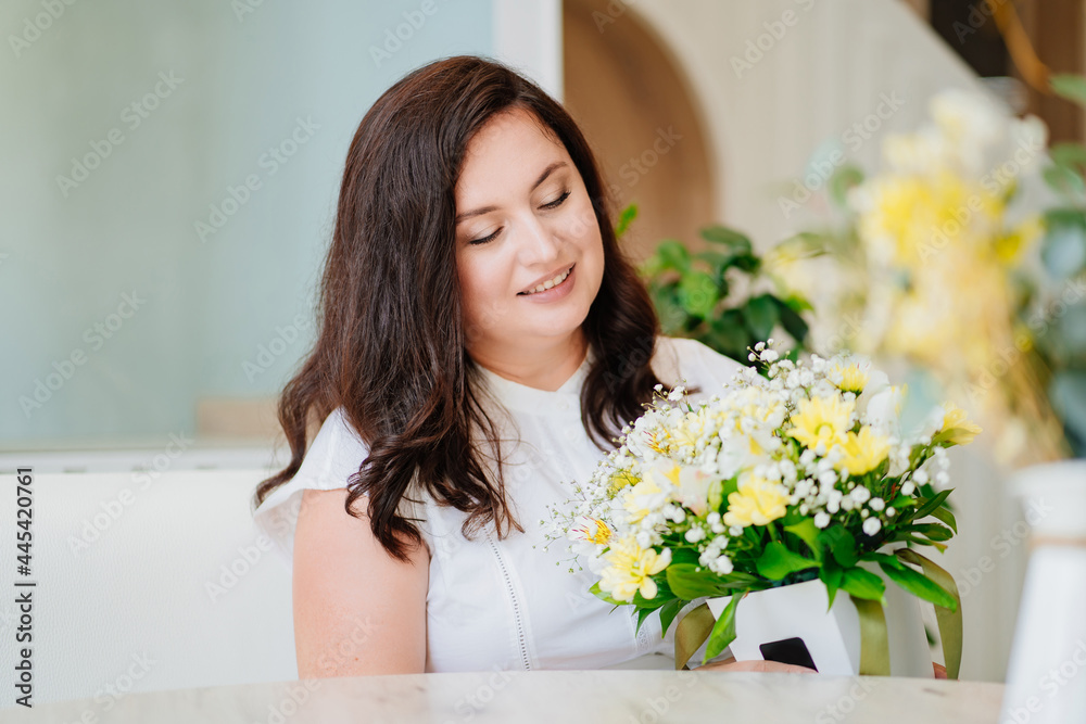 attractive woman in white clothes with flowers at the table in a light room. attractive woman in white clothes with flowers at the table in a light room.