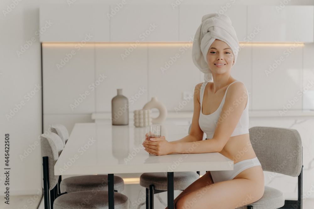 Relaxed beautıful slender woman sitting in kitchen after taking shower with glass of water Relaxed beautıful slender woman sitting in kitchen after taking shower with glass of water